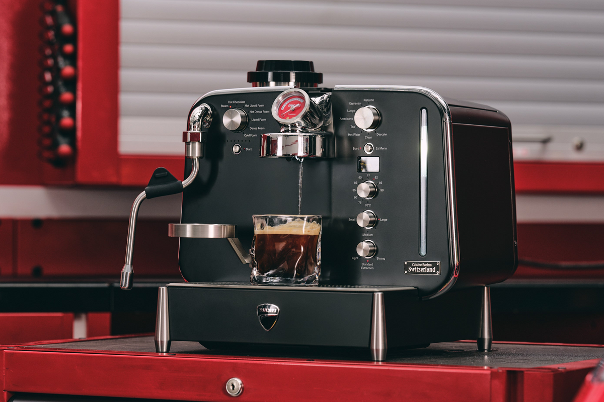 Black Barista M3 by Ducati brewing espresso into a glass on a red workshop trolley