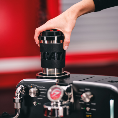 Hand placing a black Ducati travel mug in the round opening on top of the Barista M3