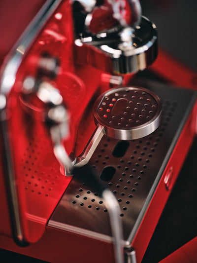 Chrome brew head and perforated stainless drip tray of the red Barista M3 seen from above