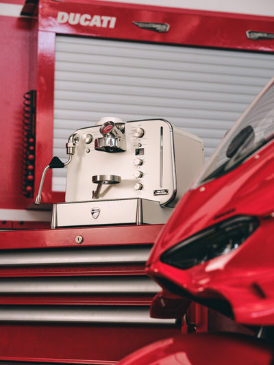 White Barista M3 on a Ducati tool cabinet with the front of a red motorcycle in the foreground