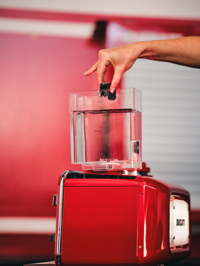 Hand lifting the clear water tank with MAX and DESCALE marks off the red Barista M3