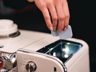 Hand dropping a grey tablet into the open compartment on top of the white Barista M3