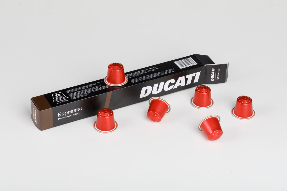 Caja Espresso by Ducati tumbada, rodeada de cápsulas rojas compatibles con Nespresso® Original