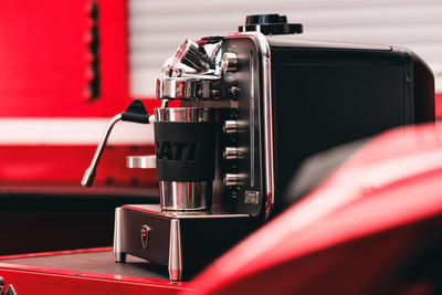 Barista M3 in black in a workshop, a steel cup in a Ducati sleeve under the brew head
